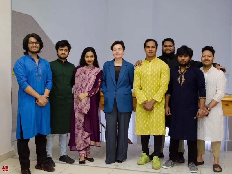 A group of seven individuals standing together in a formal setting, dressed in a mix of traditional and modern attire. They are posing for a photo, with some wearing kurta pajamas and others in suits or casual clothing.