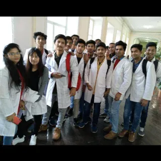 A group of students in white lab coats standing together in a hallway, posing for a photo. The setting appears to be an educational or medical institution.
